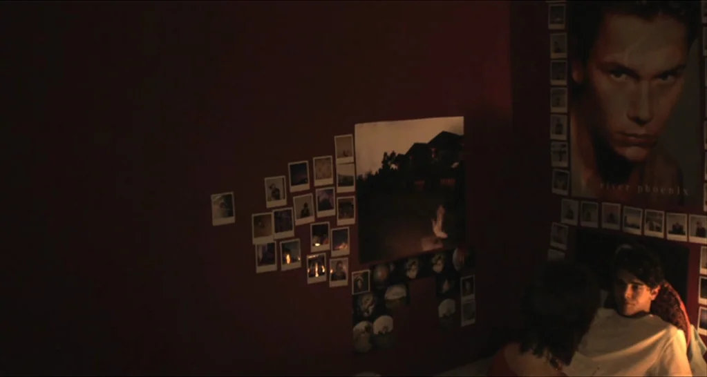 I Killed My Mother (J’ai tué ma mère) (2009) movie still: medium — A dark, dimly lit room has walls covered with numerous polaroid photos. Two…