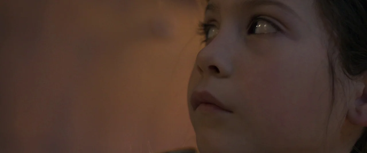 Room (2015) movie still: closeup — A close view shows a small child's face in a dimly lit, undefined space. The subject stares toward the side of…