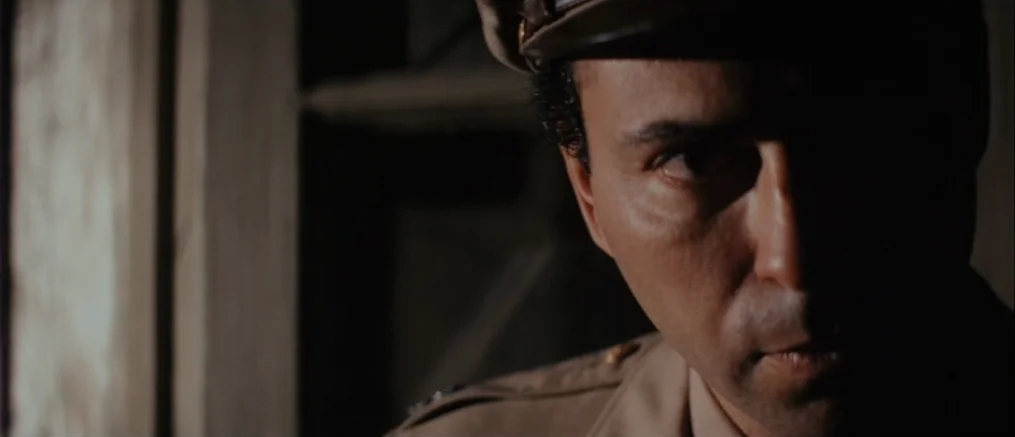 Catch 22 (1970) movie still: closeup — A dark interior space with wooden architectural elements visible in the background. A man in a military…