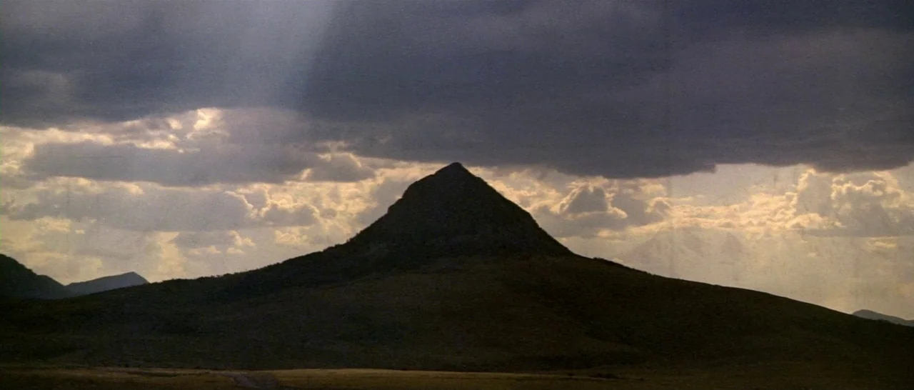 Thunderbolt & Lightfoot (1974) movie still: establishing — A dark, prominent mountain peak rises against a sky filled with heavy storm clouds.…