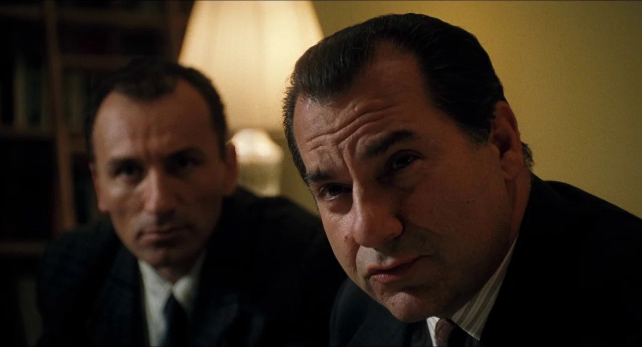 Happiness (1998) movie still: medium — An interior office with a lamp glowing behind two men in suits. The men sit side by side as they look towards…