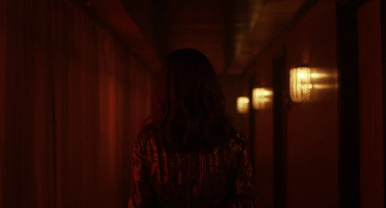 Priscilla (2023) movie still: medium — A long, dimly lit passageway features a series of warm wall sconces on one side. A person in a dark jacket…
