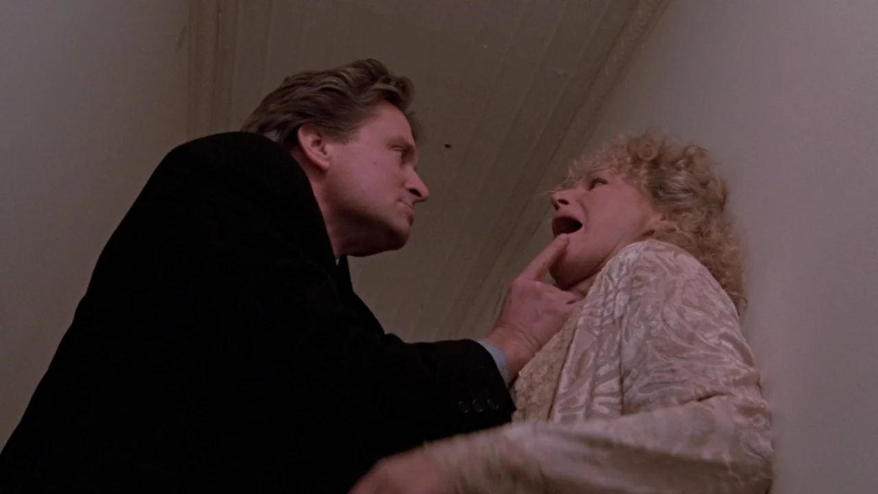 Fatal Attraction (1987) movie still: medium — Two individuals interact in a dim, narrow passageway with neutral-colored walls. The man stands over…