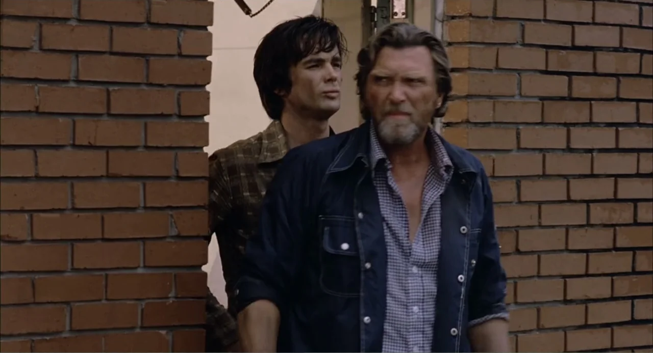 Empire of the Ants (1977) movie still: medium — Two men stand together at a building opening framed by textured red brick walls. The older man with…