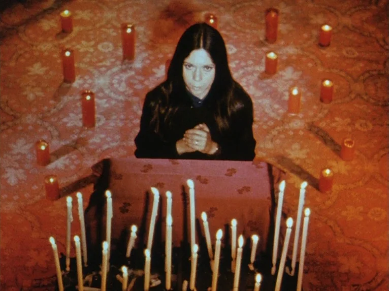 Our Lady of the Turks (1968) movie still: medium — A dark carpeted room is decorated with a pattern of red cylindrical candles. A young woman sits…