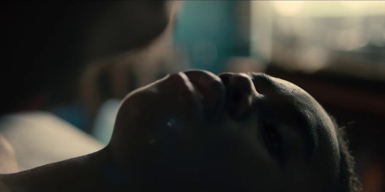 Charm City Kings (2020) movie still: closeup — A close-up view of a person lying on their back in a dimly lit room. The subject's face is partially…