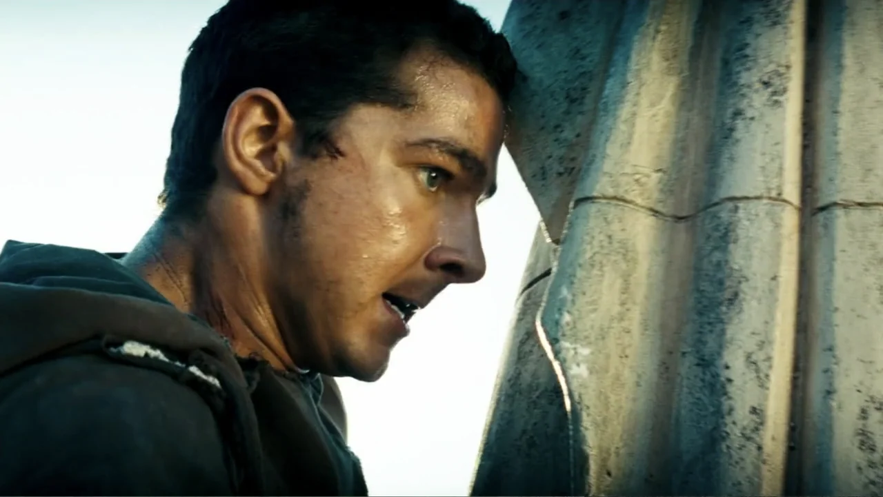 Transformers (2007) movie still: closeup — A man stands outdoors pressing his face against the side of a stone structure. The man is sweating and…