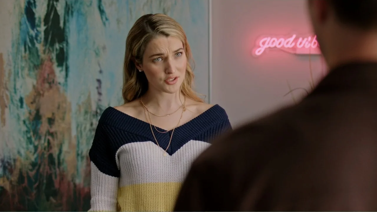 Ghosts of Christmas Past (2021) movie still: medium — An interior space features a large abstract painting and a pink neon sign. A young blonde…