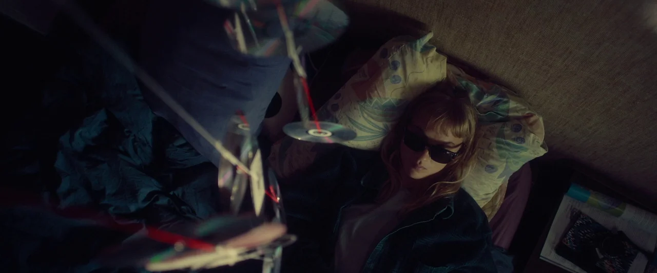 Meanwhile On Earth (2024) movie still: medium — A dimly lit bedroom features a person resting on a patterned pillow. Several shiny compact discs…