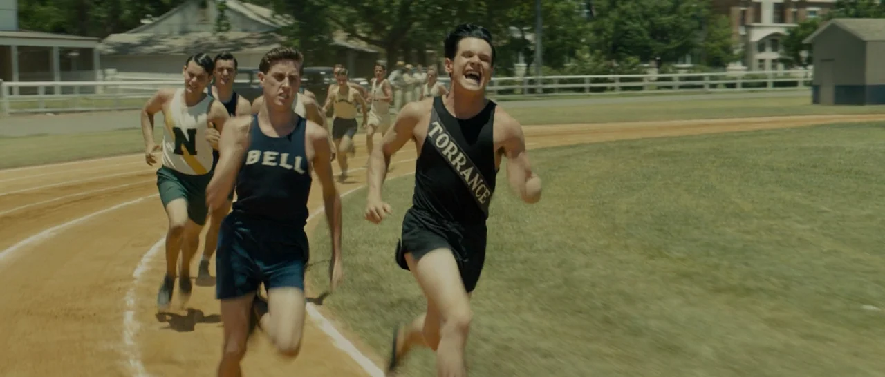 Unbroken (2014) movie still: fullbody — An outdoor running track features multiple young men in period athletic gear competing together. The runners…