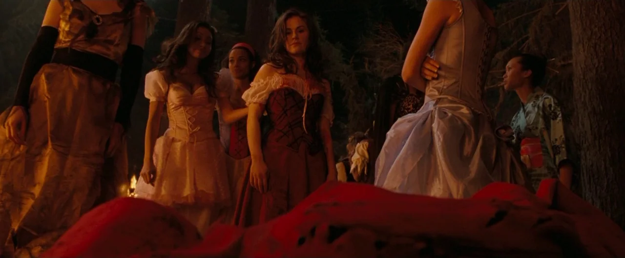 Trick ‘R Treat (2007) movie still: medium — A group of women in varied dresses stands in a dark wooded area at night. The women gather in a circle…