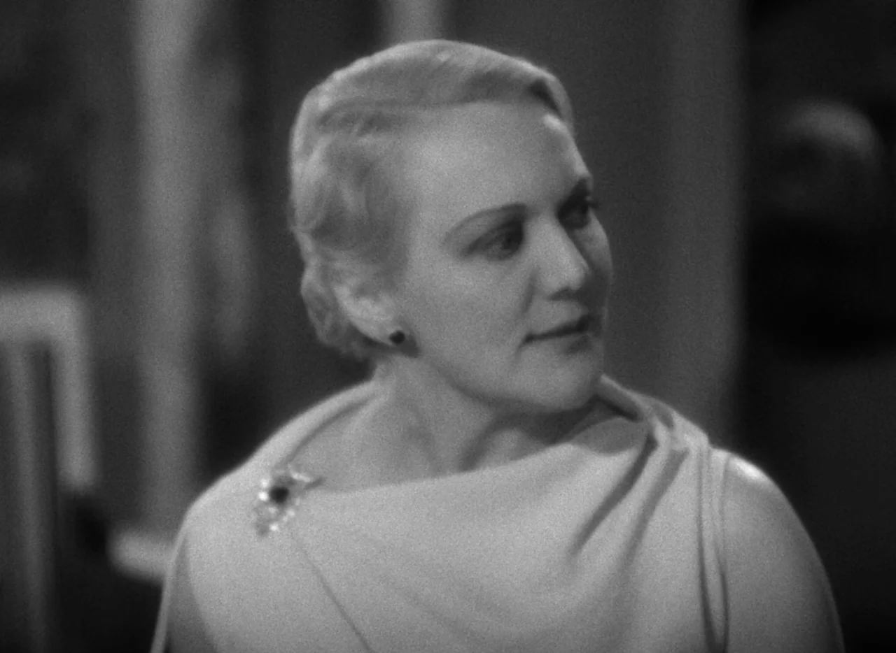 The Thin Man (1934) movie still: closeup — An interior space features a woman in an elegant, light-colored draped evening gown. She turns her head…