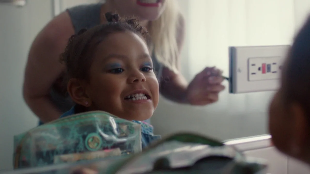 Saint Frances (2019) movie still: closeup — A brightly lit bathroom with a mirror reflecting the faces of a child and woman. The child gazes into…