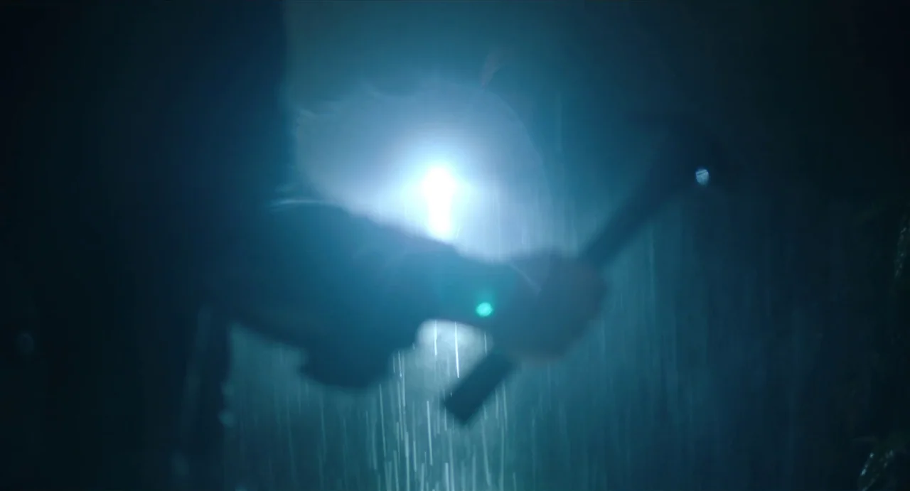 May The Devil Take You (2018) movie still: closeup — A dark, rainy outdoor environment lit by a powerful, hazy light source from behind. A…