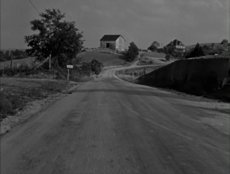 The Night Of The Hunter (1955) movie still: establishing — A paved rural road stretches toward a small house perched on a rolling hill. Grassy…