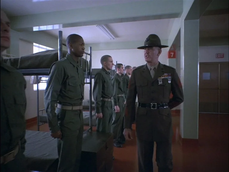 Full Metal Jacket (1987) movie still: fullbody — A military barracks interior features metal bunk beds and plain painted walls. A drill instructor…