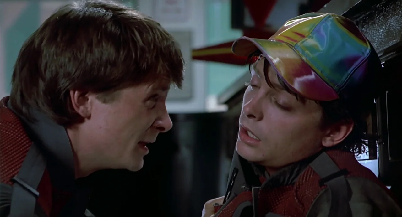 Back to the Future II (1989) movie still: medium — Two identical men stand face-to-face inside a brightly lit indoor space. They are wearing…