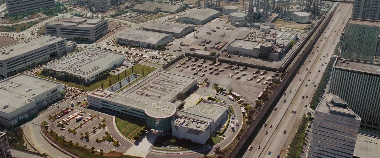 Iron Man (2008) movie still: establishing — An aerial view displays a sprawling industrial complex with multiple large warehouses and buildings. A…