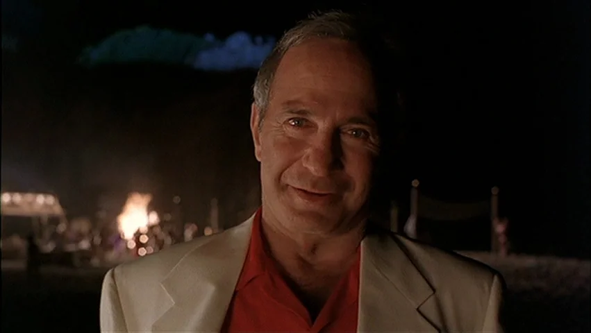 The Big Lebowski (1998) movie still: closeup — An outdoor night environment features a dark, blurry background with a distant campfire. A man in a…