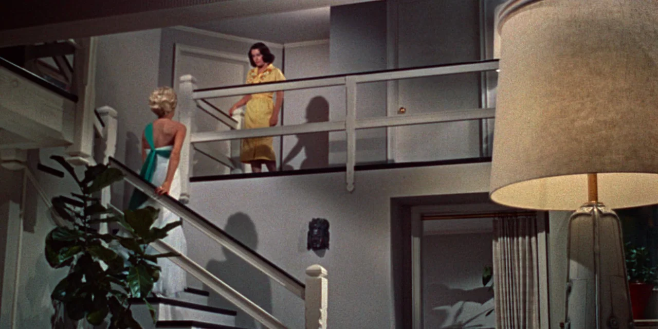 Imitation of Life (1959) movie still: wide — A split-level home interior features a white wooden staircase and a landing walkway. One woman ascends…