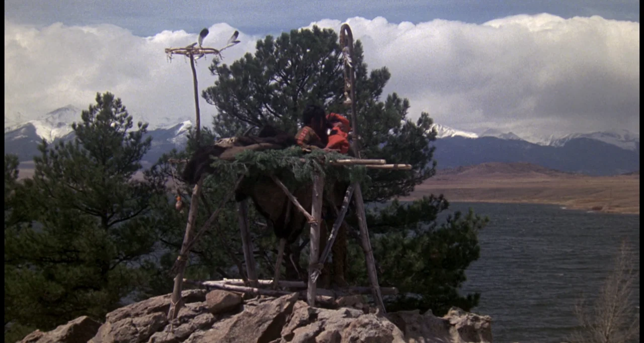The White Buffalo (1977) movie still: wide — A wooden platform stands on a craggy hilltop overlooking a large body of water. A man sits atop the…