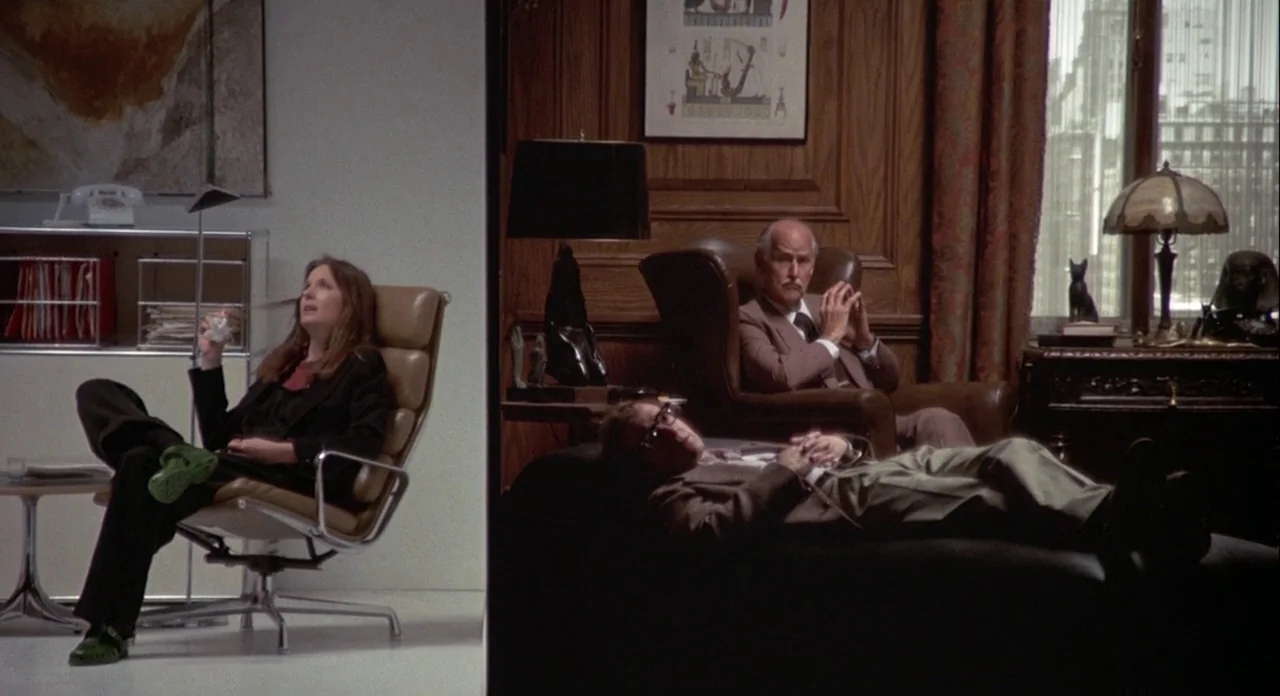 Annie Hall (1977) movie still: wide — The frame is split between a bright, minimalist white office and a dark, wood-paneled room. Three people are…