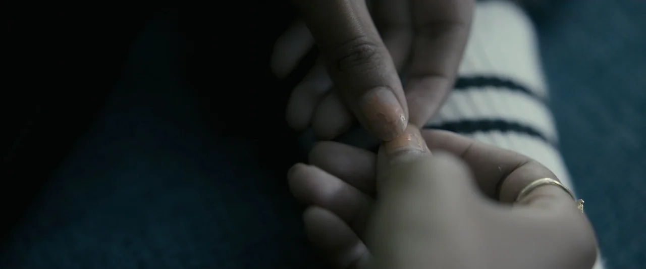 Talk to Me (2023) movie still: closeup — A close view shows two people's hands touching against a dark fabric background. One person wears a thin…