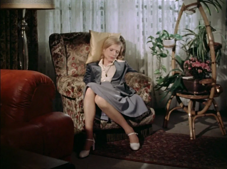 Fear Of Fear (1975) movie still: medium — A furnished interior featuring a floral armchair and a bamboo plant stand. A woman sits in the chair with…