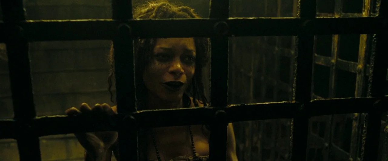 Pirates of the Caribbean: At World’s End movie still: closeup — A dark space defined by thick iron bars and deep shadows. A woman looks forward…