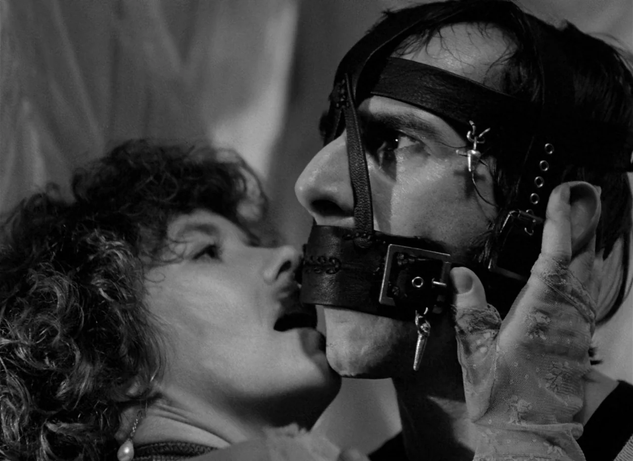 Singapore Sling (1990) movie still: closeup — An interior space features two figures captured in a tight, monochromatic close-up. A woman leans in…