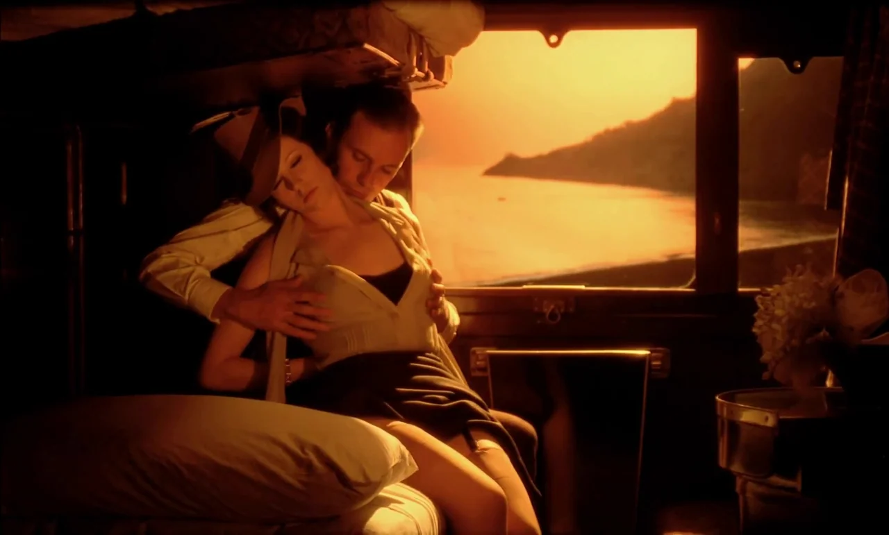 The Conformist (1970) movie still: medium — A vintage wood-paneled train sleeping compartment with a large window looking out at dusk. A man and a…