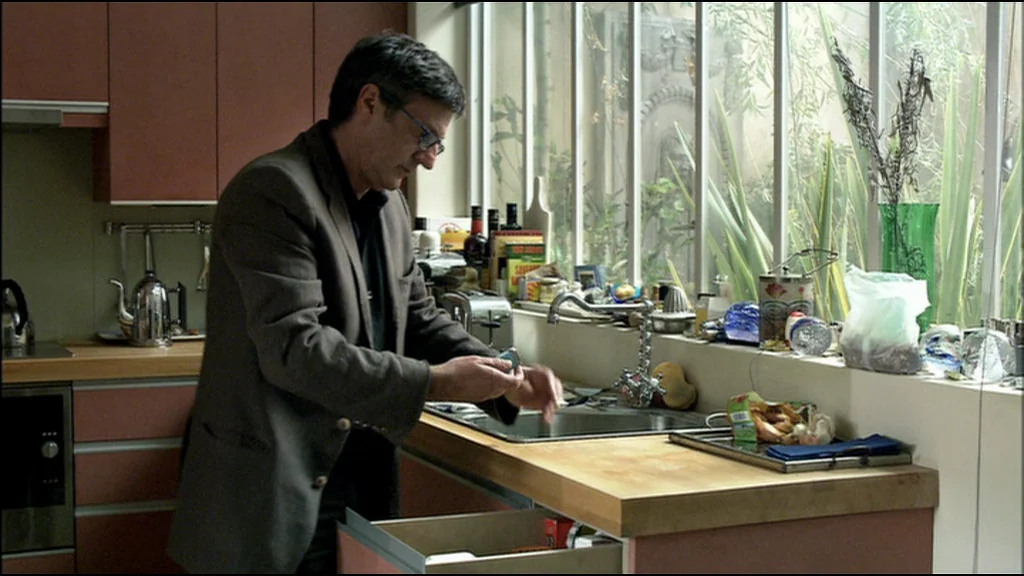 Caché (Hidden) (2005) movie still: medium — A kitchen with dark cabinetry and a wooden countertop sits before a large window. A man in a blazer…