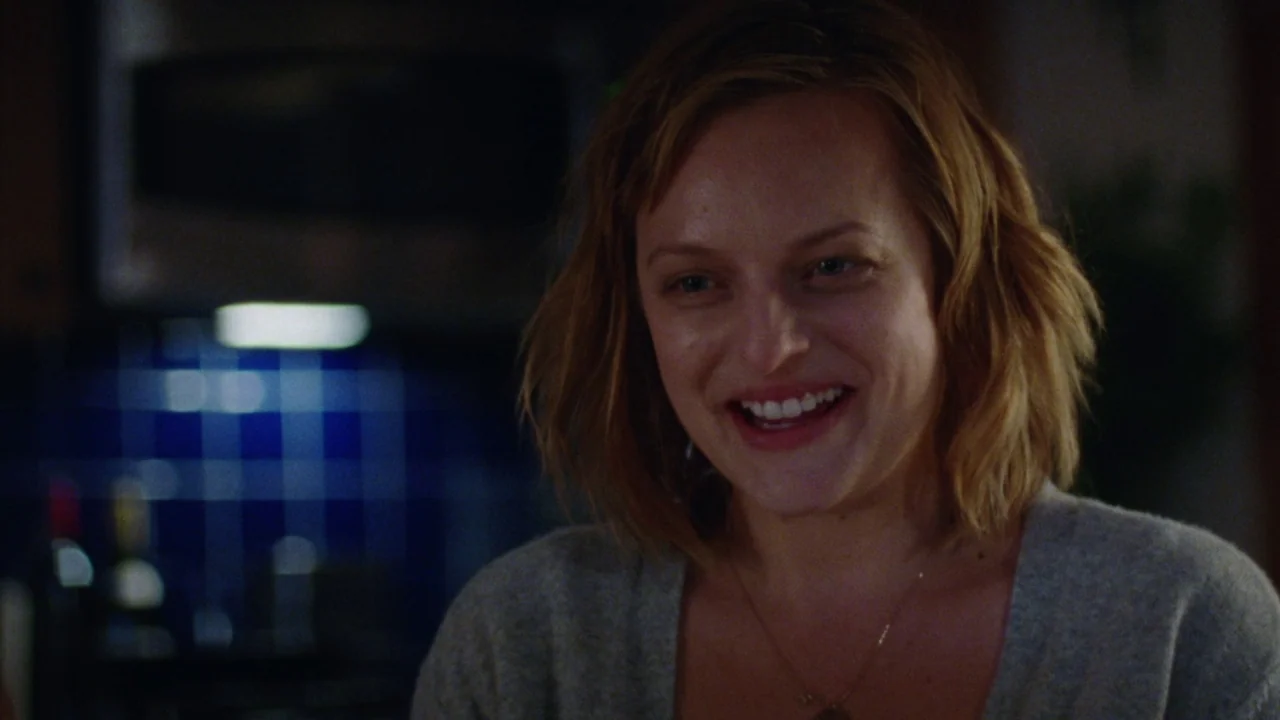 Queen of Earth (2015) movie still: closeup — A dark kitchen interior featuring a wall of blue square tiles in the background. A woman in a grey…