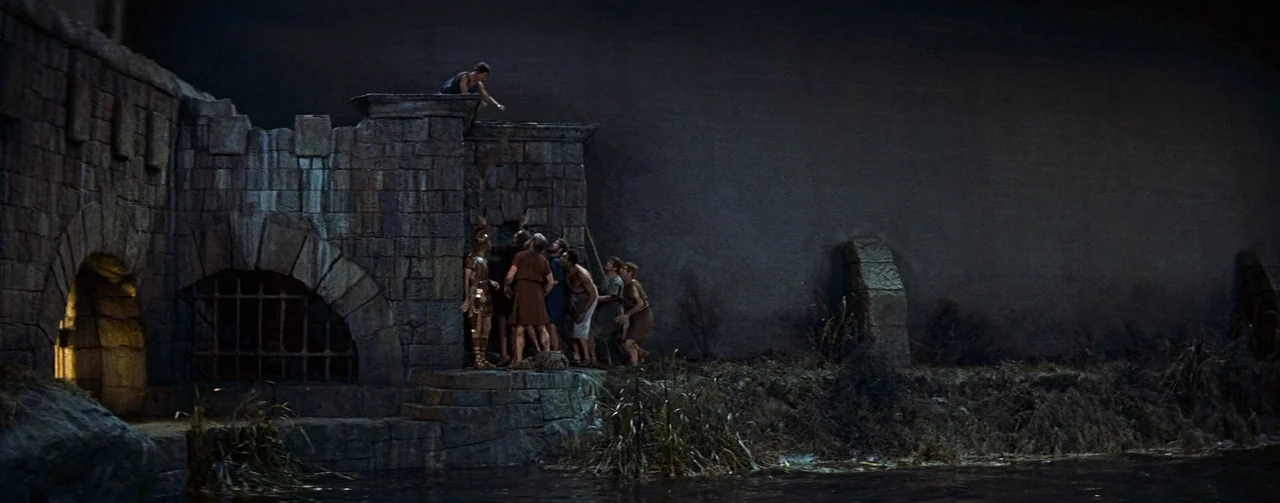 The Robe (1953) movie still: wide — A stone fortification stands along a dark water channel under a night sky. A group of men in ancient attire…