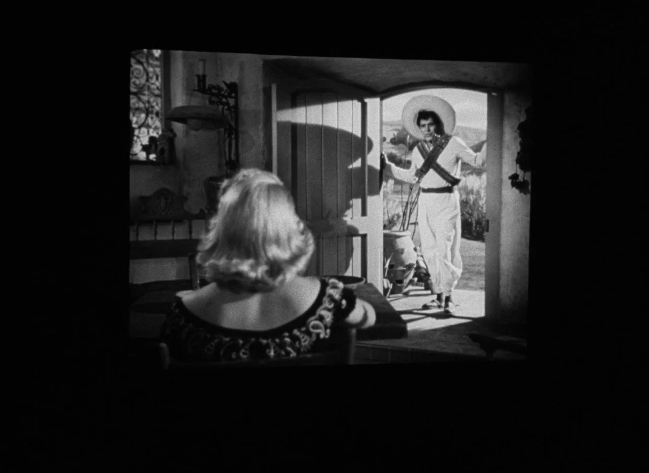 The Bad and the Beautiful (1952) movie still: medium — A dimly lit room with stone walls and wooden furniture faces an outdoor courtyard. A woman…
