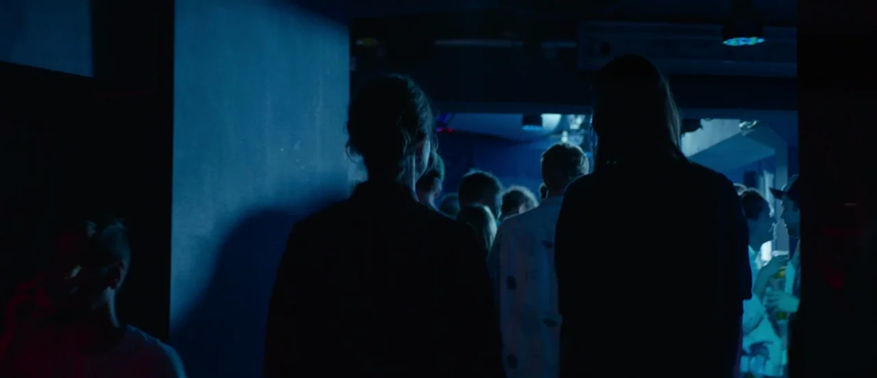 Thelma (2017) movie still: medium — A crowded, dimly lit indoor space with low ceilings and dark walls. Several figures stand in silhouettes, facing…