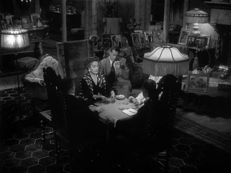 Sunset Boulevard (1950) movie still: wide — An opulent, cluttered interior room with hexagonal floor tiles and numerous framed photographs. Four…