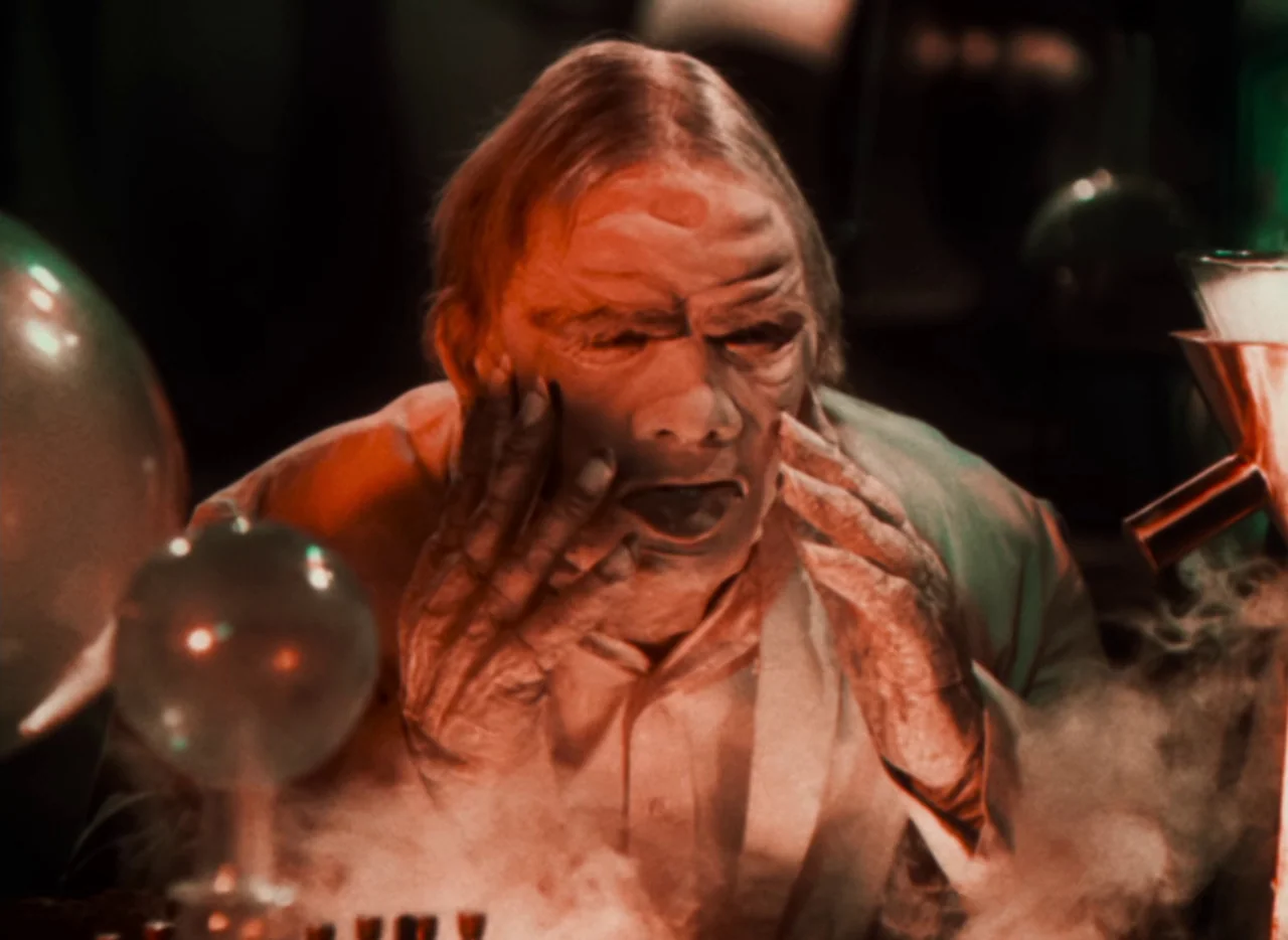 Doctor X (1932) movie still: closeup — A dark, atmospheric space contains scientific glass apparatus and thick billowing smoke. An elderly man with…