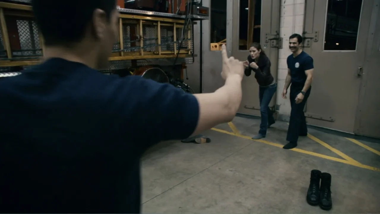 Quarantine (2008) movie still: medium — A fire station equipment bay with large overhead doors and ladders mounted on walls. A man points his finger…