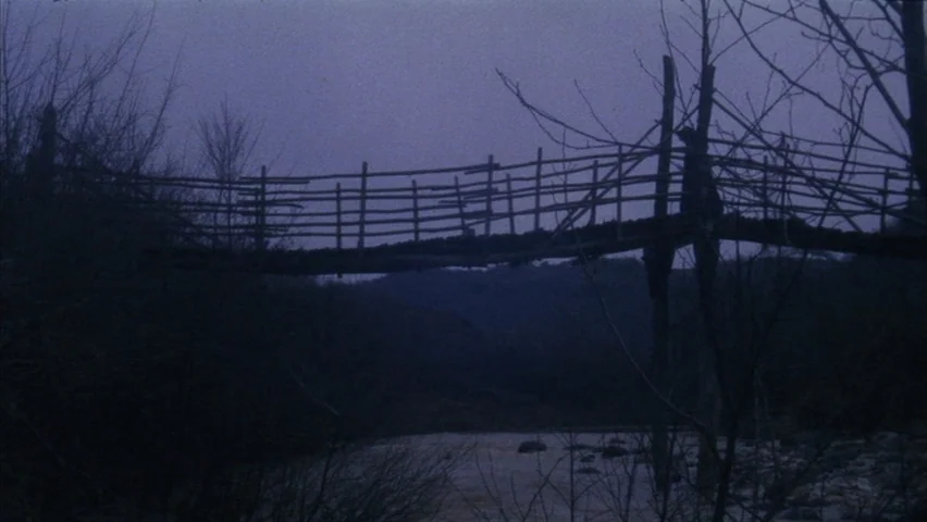 Black Sabbath (1963) movie still: wide — A makeshift wooden bridge spans across a dark, flowing river at twilight. The bridge is constructed of…