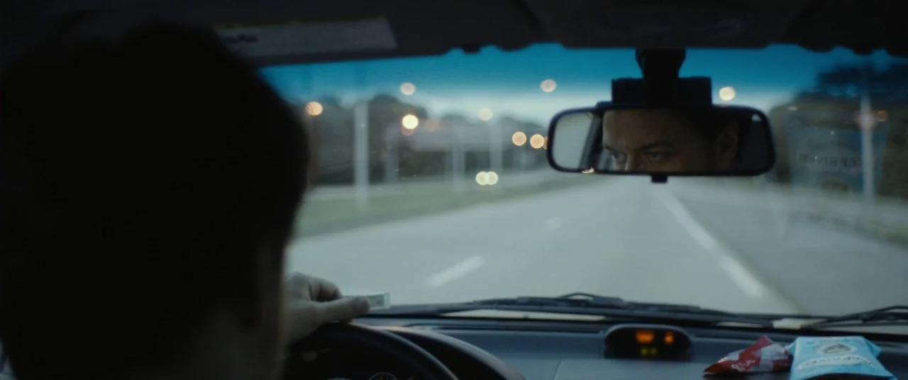 The Disappearance of Eleanor Rigby: Him (2014) movie still: A tense, atmospheric shot from inside a car at dusk, focusing on a man's intense gaze…