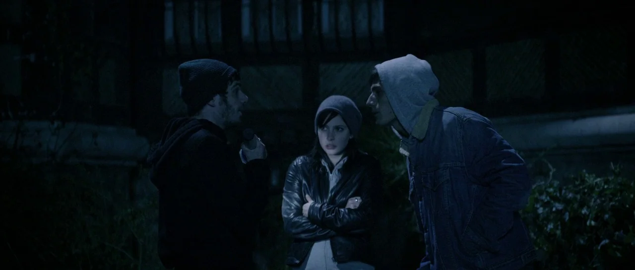 Livid (2011) movie still: medium — An outdoor area at night featuring a dark building facade with visible architectural details. Three young adults…