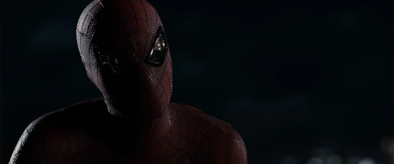 The Amazing Spider-Man (2012) movie still: closeup — A dark night exterior set on a high rooftop against a black background. A masked superhero in a…
