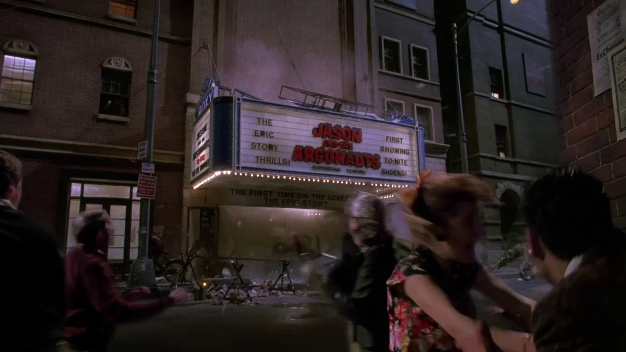 Little Shop of Horrors (1986) movie still: wide — A brick movie theater facade displays a marquee for Jason and the Argonauts at night. People on…