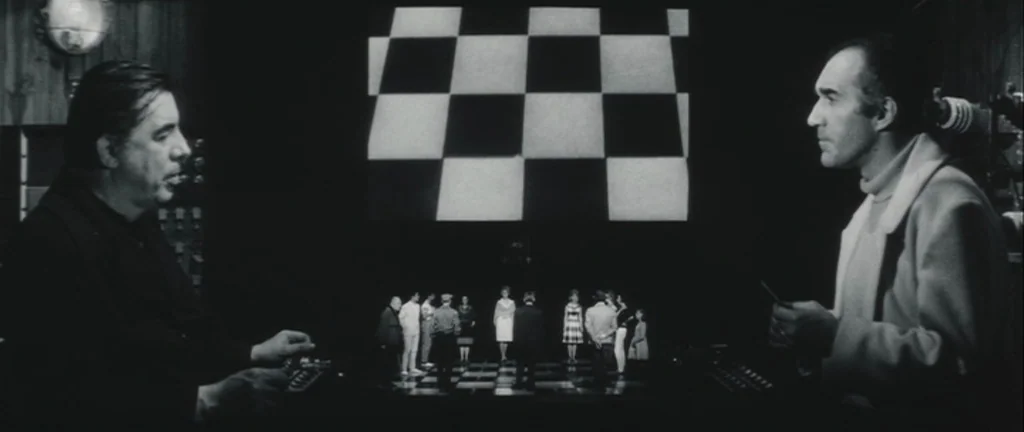 Les Créatures (1966) movie still: wide — A dark, spartan control room looks out over a checkered floor with small figures. Two men stand in the…