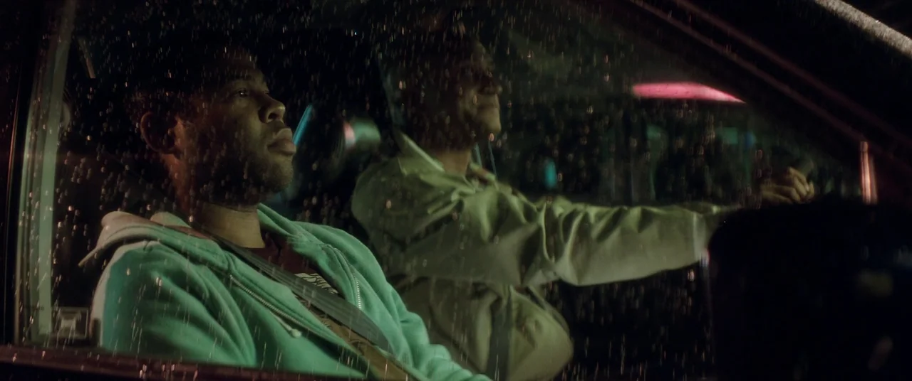 Keanu (2016) movie still: medium — A dark car interior at night with rain droplets covering the glass surface. Two men sit side by side in the front…