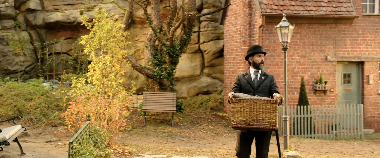 Jim Button and Luke the Engine Driver (2018) movie still: fullbody — A residential courtyard features a red brick cottage, a stone cliff, and wooden…