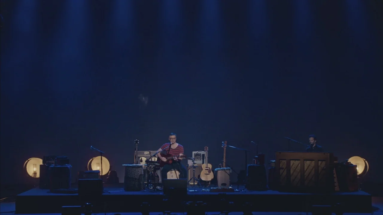 Flight of the Conchords: Live in London (2018) movie still: wide — A dark concert stage is illuminated by several low-lying round stage lamps. Two…