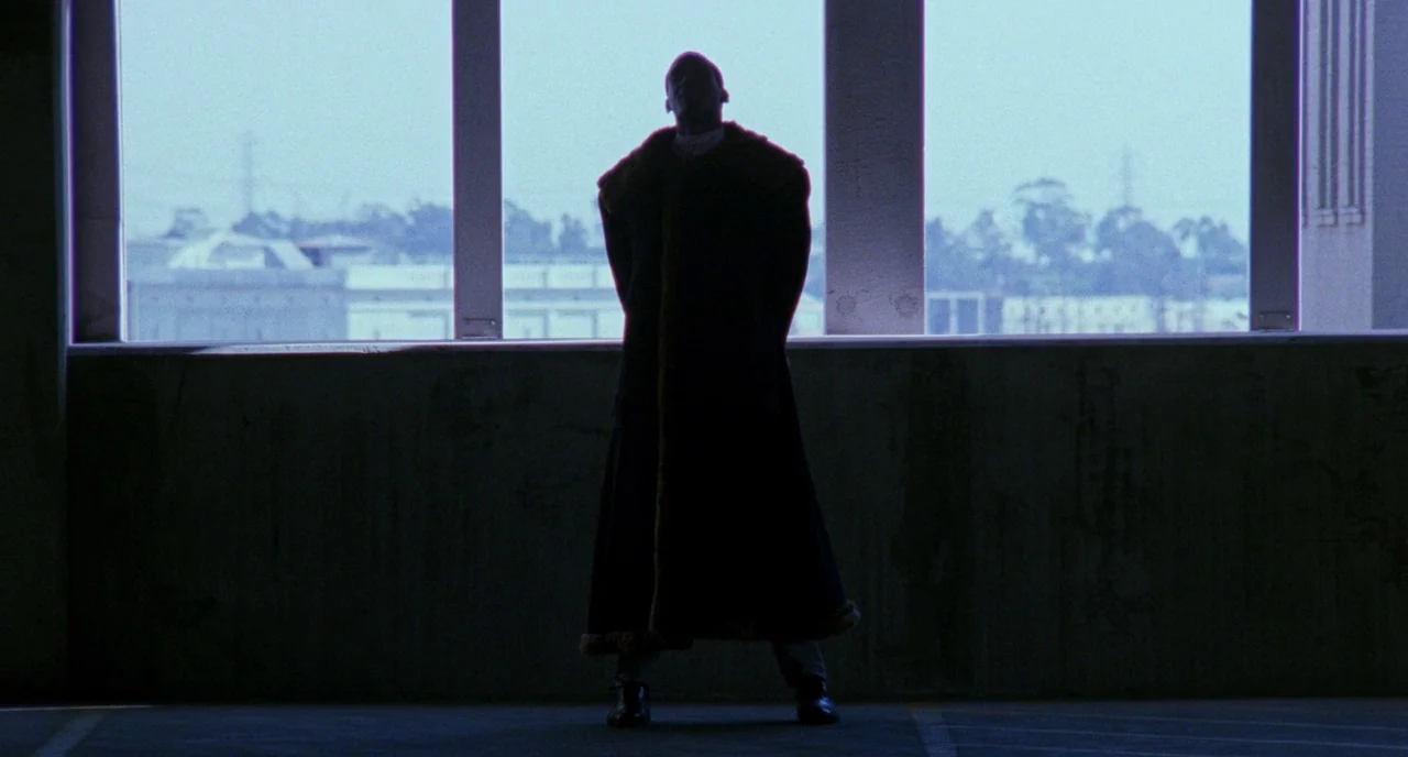 Candyman (1992) movie still: fullbody — A concrete parking structure features a wide window overlooking a distant urban horizon. A solitary man…