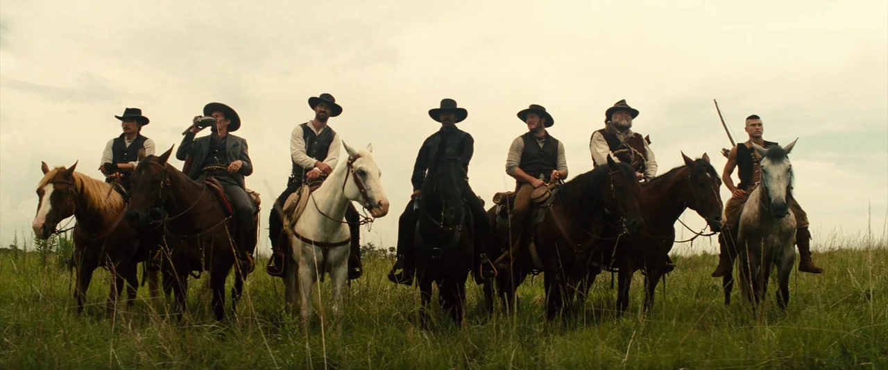 The Magnificent Seven (2016) (2016) movie still: fullbody — A group of seven men sit on horses in a wide grassy field. The men are dressed in…